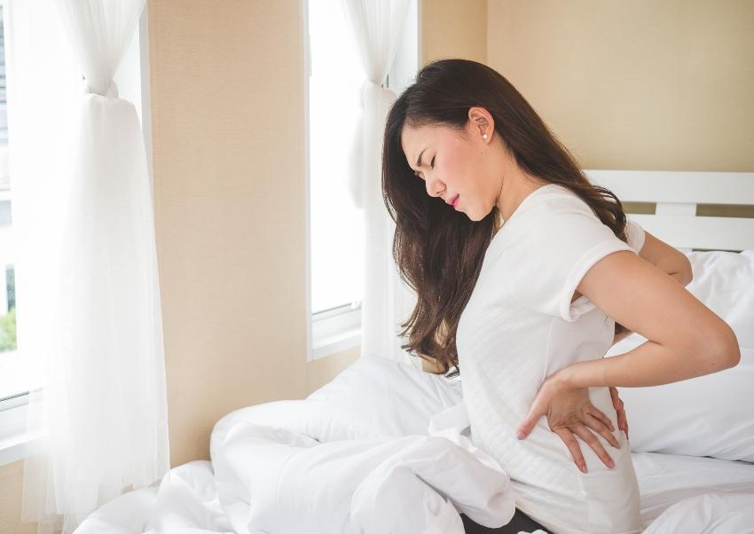 Junge Frau mit Rückenschmerzen, sitzend auf einem Bett