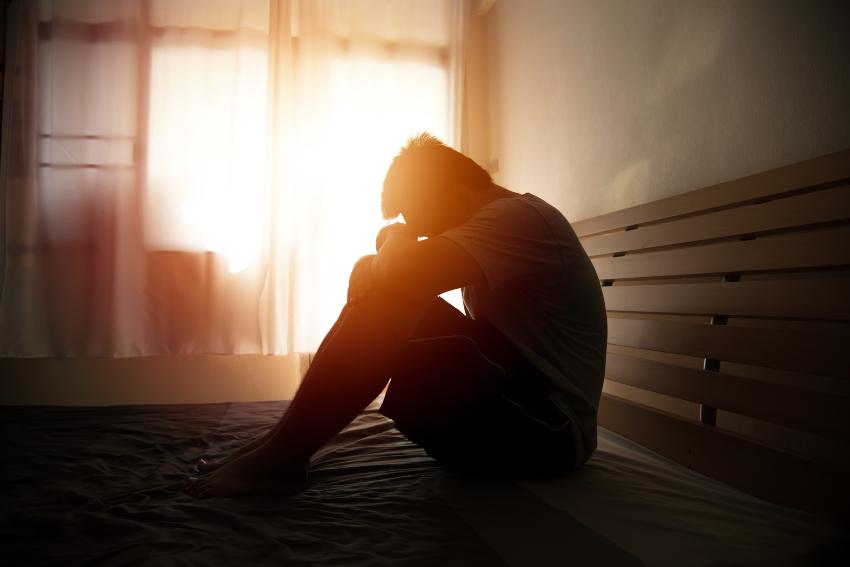 Junger Mann kauert auf seinem Bett - Depression als Symptom beim Kleine-Levin-Syndrom