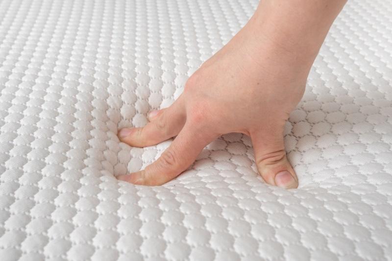 Ein Hand prüft die Elastizität einer Matratze, indem sie kräftig auf Oberfläche drückt Punktelastizität bei Matratzen