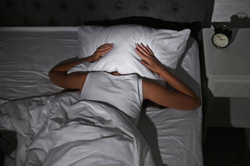 Junge Frau kann nicht schlafen, sie hat ein Kissen über den Kopf gelegt - Unruhiger Schlaf