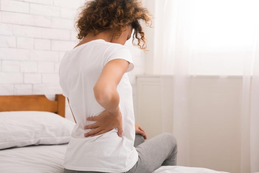 Junge Frau im Bet mit Rückenschmerzen - Rückenschonende Matratzen können helfen