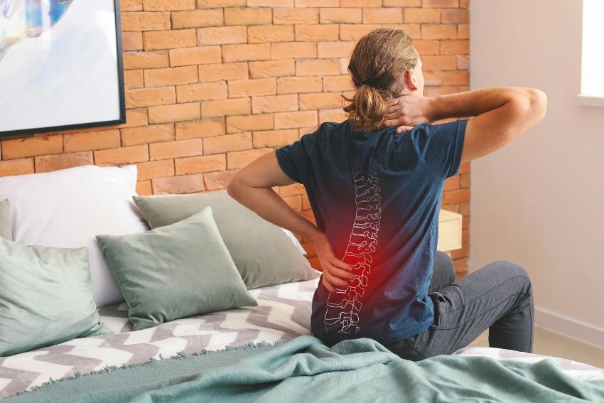 Junger Mann sitzt im Bett mit Rückenschmerzen - Rückenschonende Matratzen können helfen