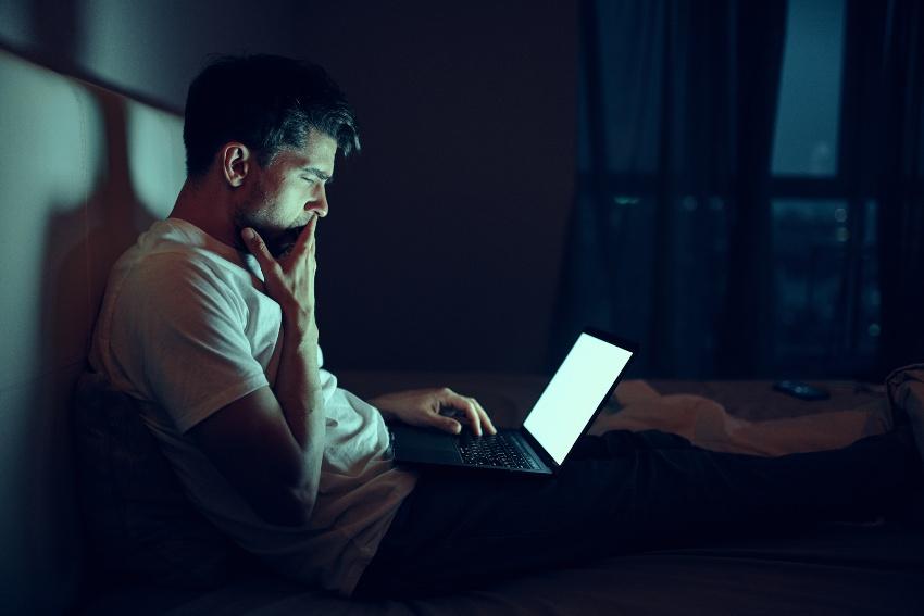 Junger Mann abends im Bett am Laptop