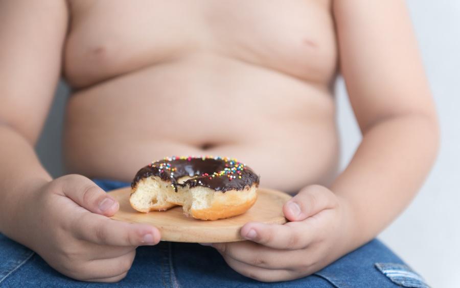 Dickes Kind mit Doughnut in der Hand - Schlafmangel und Übergewicht