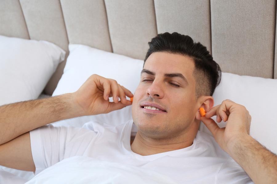Junger Mann steckt sich Ohrenstöpsel in die Ohren - Erste-Nacht-Effekt bekämpfen