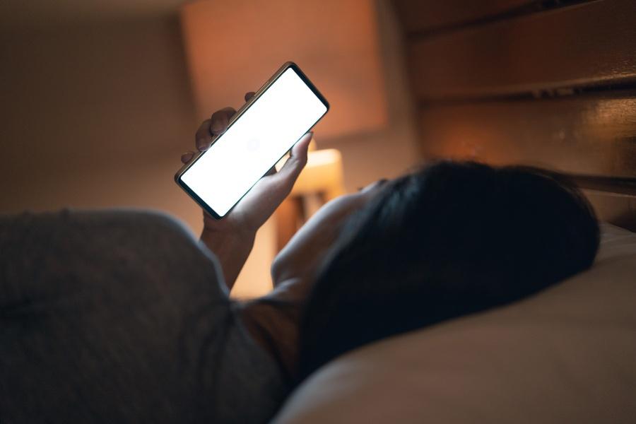Junge Frau im Bett schaut auf das helle Display eines Handys