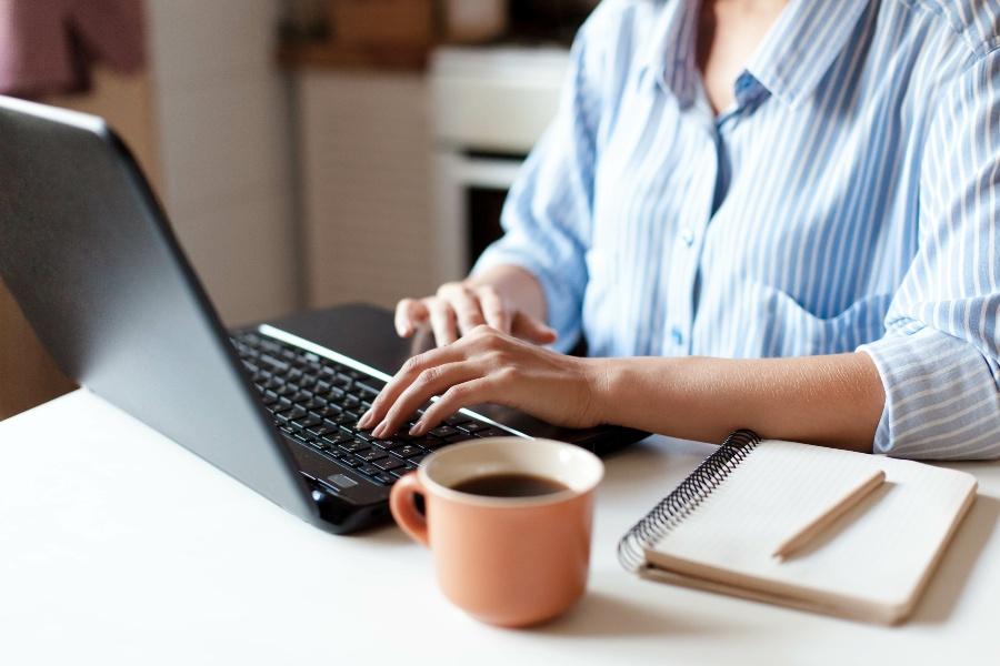 Junge Frau arbeitet am Laptop, daneben steht ein Becher mit Kaffee
