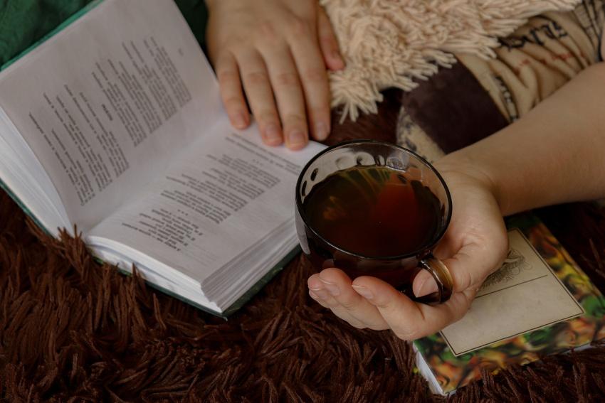Jemand liest im Bett ein Buch und trinkt Tee - Besser durchschlafen durch Rituale