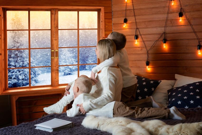 Mutter mit 2 Kindern sitzt im Bett und schaut heraus in eine Winterlandschaft