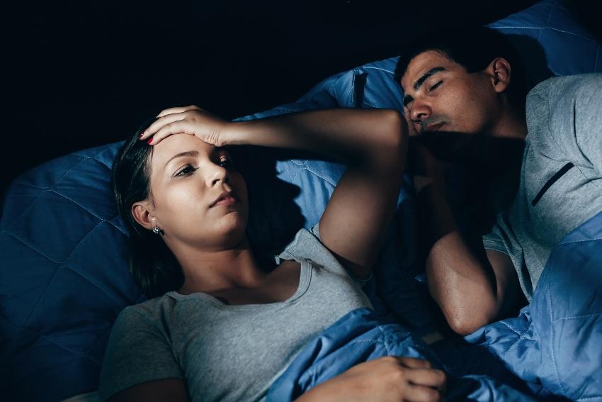 Junges Paar im Bett, Mann schläft, Frau ist wach - Die ideale Schlafenszeit