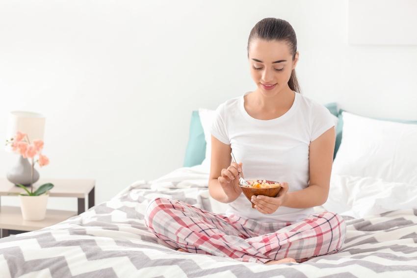Junge Frau isst morgens Müsli im Bett - morgens besser wach werden