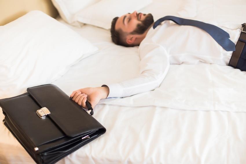 Mann in Business-Outfit liegt auf einem Hotelbett - Jetlag vermeiden