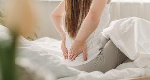 Junge Frau im Bett mit Rückenschmerzen - vielleicht Matratze durchgelegen