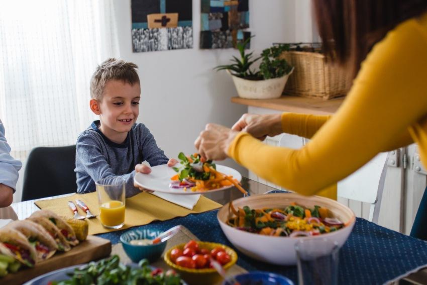 Mutter reicht Kind Salat am Tisch - Wann und was vor dem Schlafen essen?