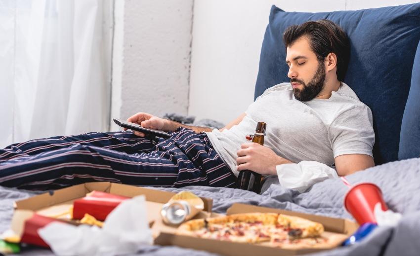 Mann liegt im Bett mit Bierflasche in der Hand