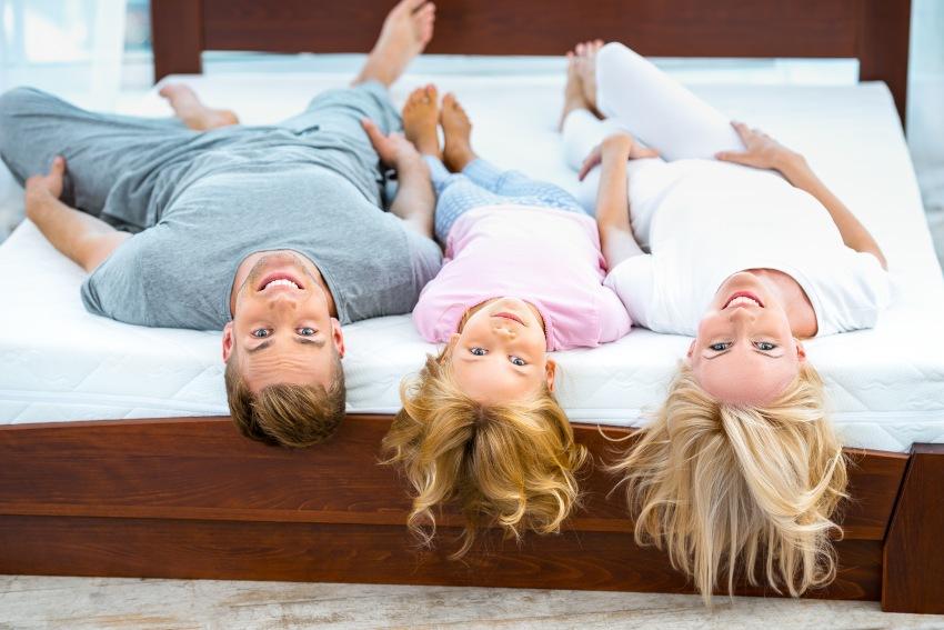 Junge Familie mit Tochter liegt gemeinsam auf einem großen Bett - Welche Matratze für welches Gewicht?