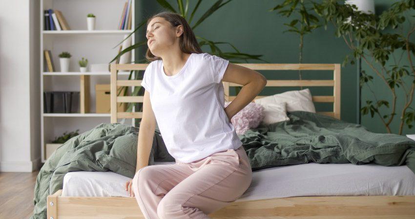 Junge Frau hat Rückenschmerzen durch ihr Bett - Wie lange ist eine Matratze haltbar