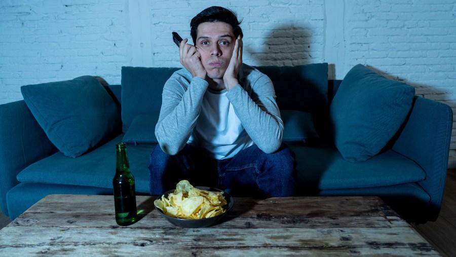 Junger Mann mit Bier und Chips vor dem Fernseher