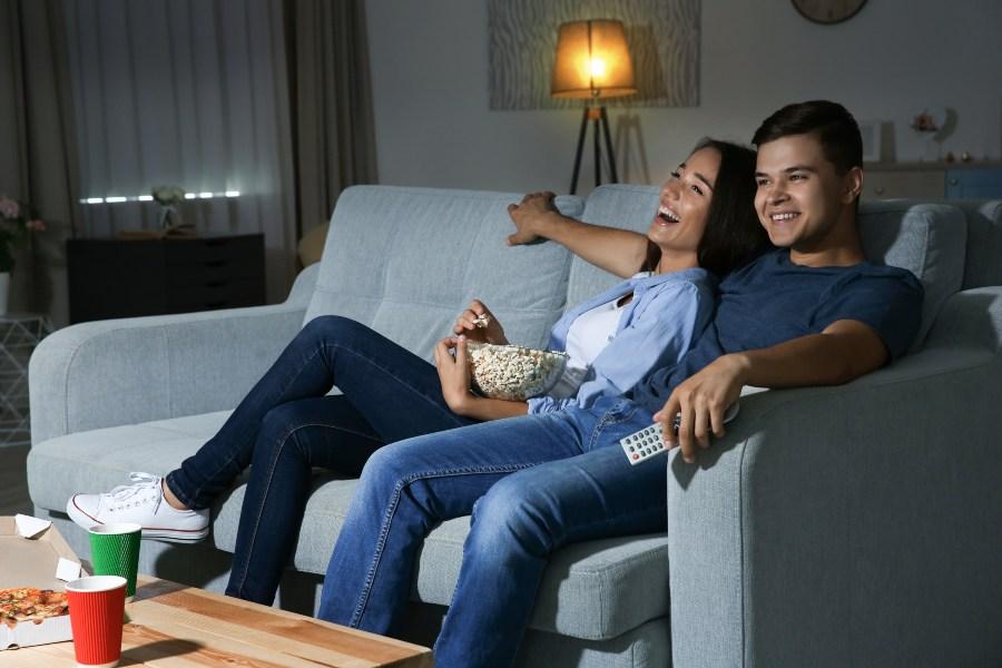 Junges Paar schaut abends fern auf der Couch - Schlafrhythmus umstellen durch Routine