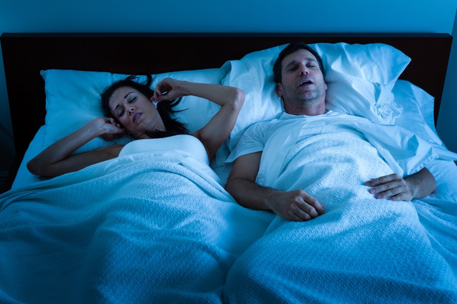 Ehepaar liegt im Bett, Mann schnarcht - Auf dem Rücken schlafen lernen