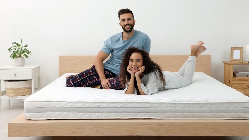 Junges Paar sitzt bzw. liegt auf einer großen Matratze im Doppelbett