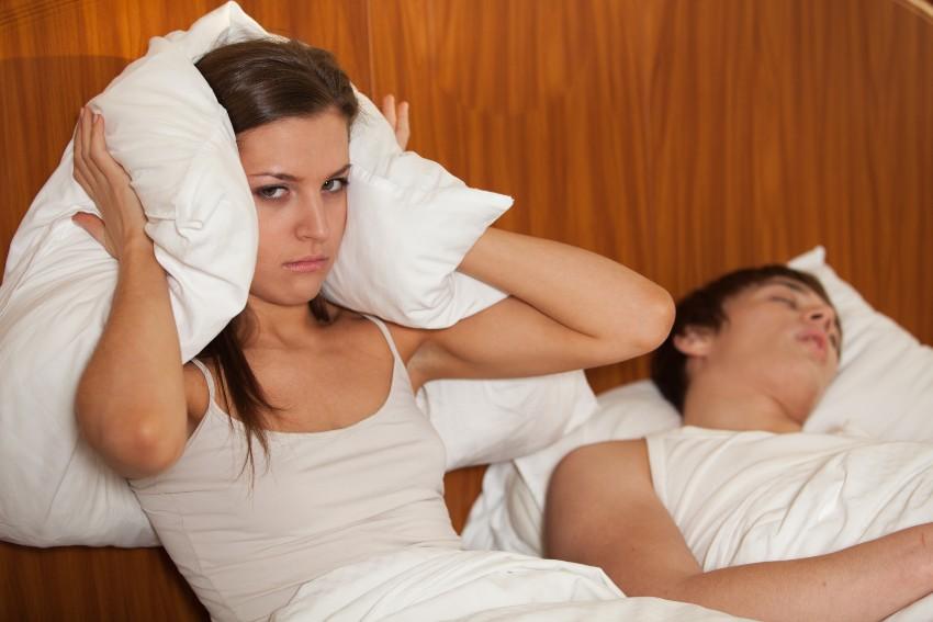 Frau hält sich Kissen an die Ohren weil der Partner schnarcht - Mann hat Schnarchprobleme