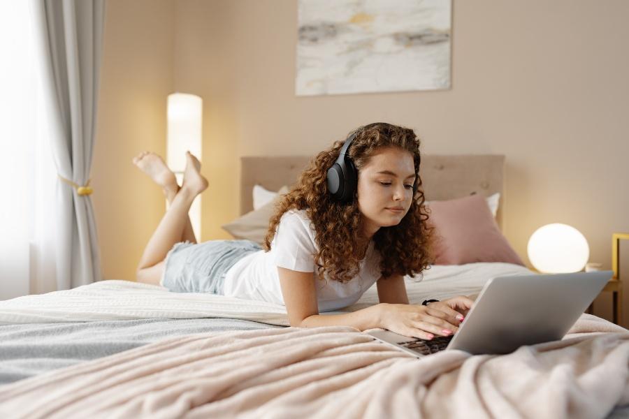 Junge Frau liegt im Bett, ist mit Laptop beschäftigt