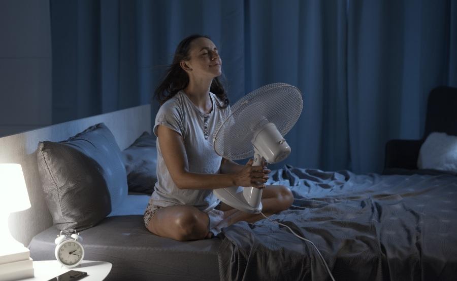 Junge Frau nutzt Ventilator im Bett - Matratze zu warm
