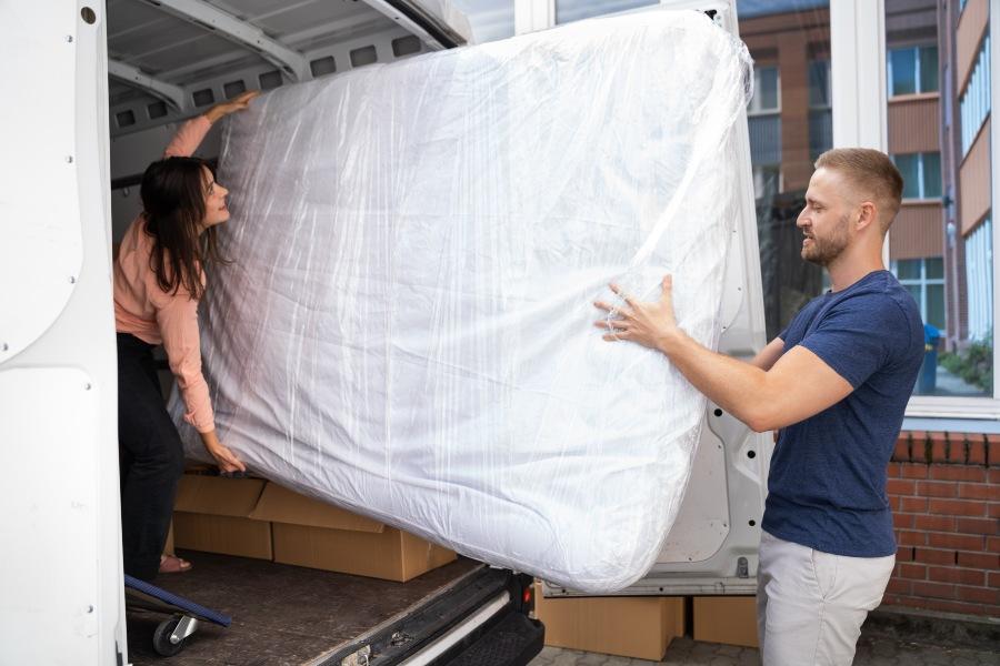 Paar trägt Matratze in einen Kleintransporter - Matratze transportieren beim Umzug