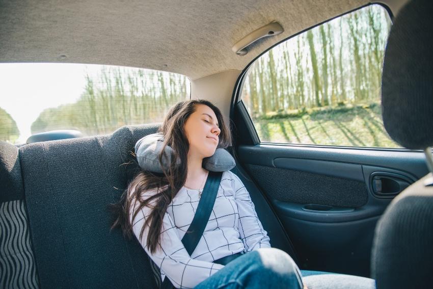 Junge Frau schläft hinten im Auto mit Nackenhörnchen