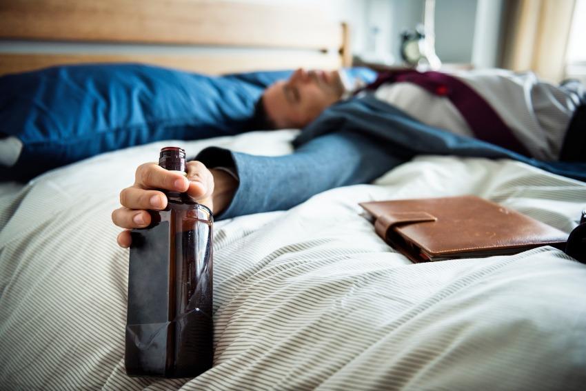 Mann liegt mit Flasche Alkohol in der Hand im Bett